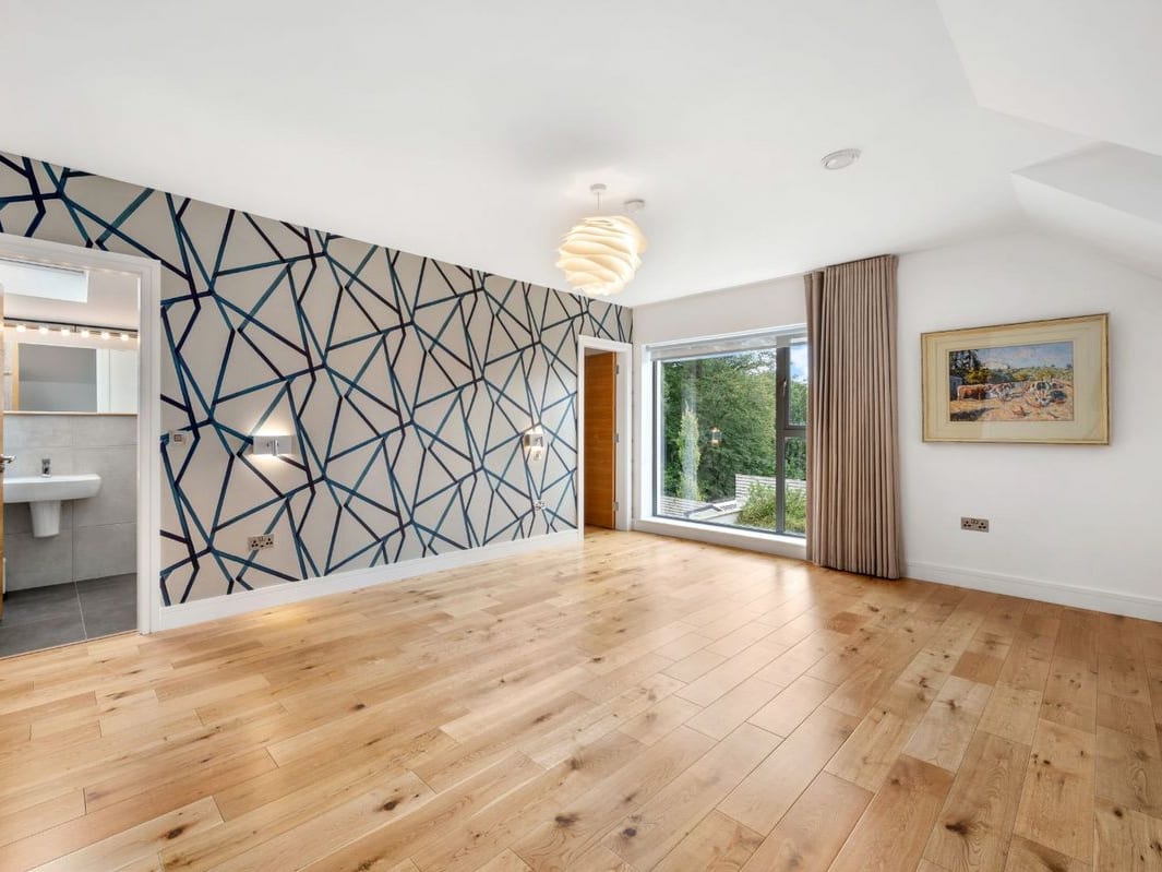 An empty bedroom with a navy geometric feature wall, an open ensuite door and a full-height window