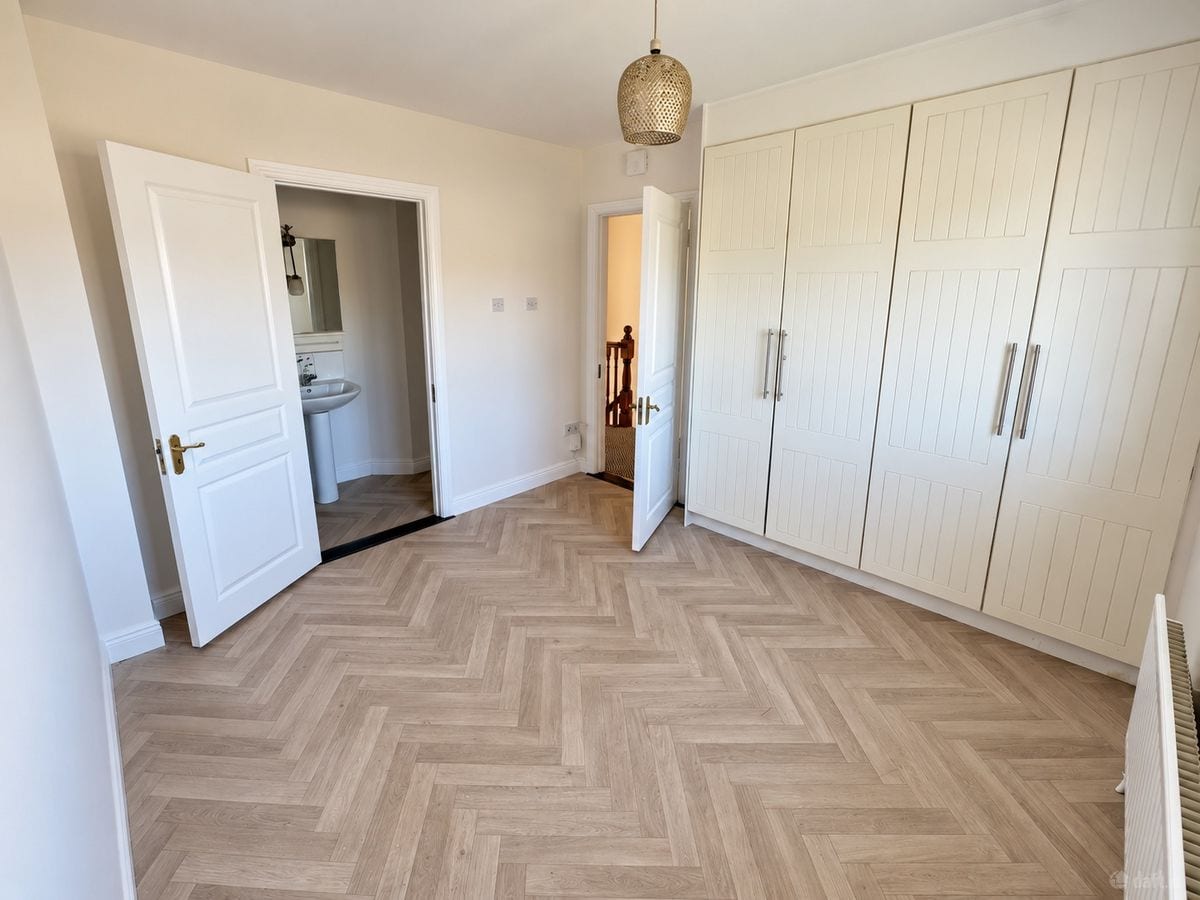 An empty bedroom with a herringbone floor, fitted cream wardrobes and two open doors