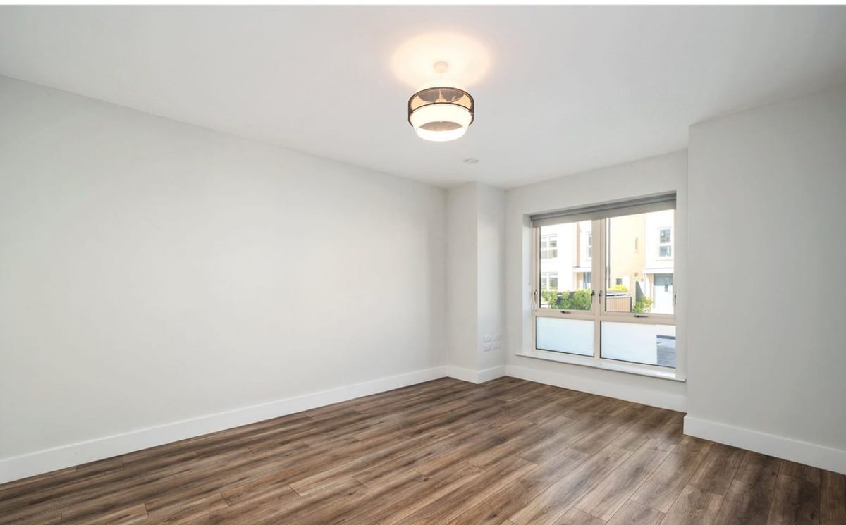 An empty living room with bare walls, a window and a wood floor