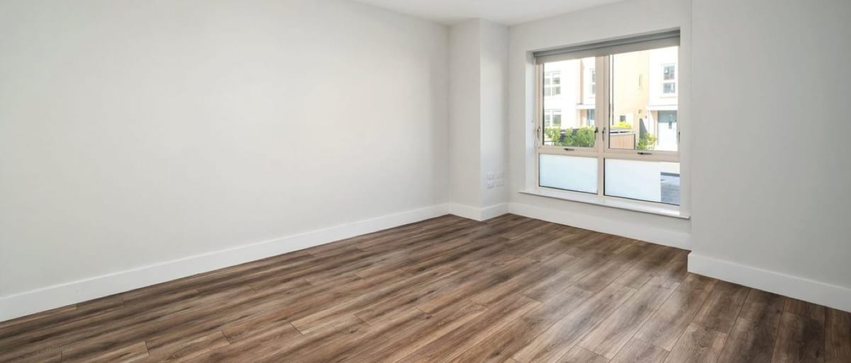 An empty living room with bare walls, a window and a wood floor