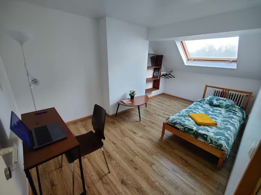 A sparse attic bedroom before redesign, with a desk, single bed and skylight under a sloped ceiling