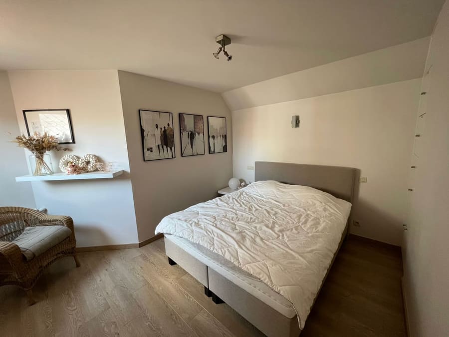 A plain bedroom before redesign, with bare walls, a sloped ceiling and a simple upholstered bed