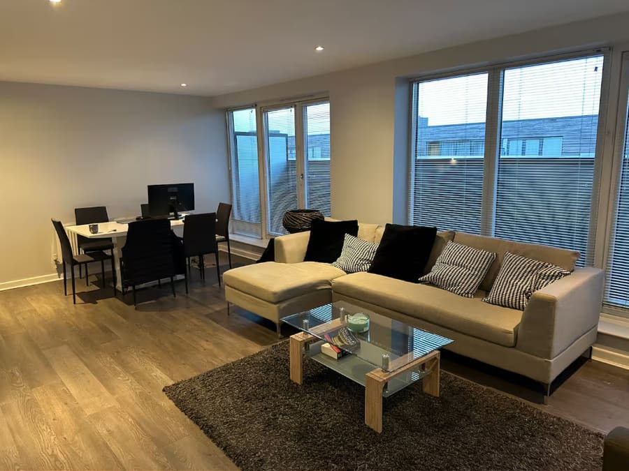 An open-plan living and dining room before redesign, with a grey corner sofa, glass coffee table and black dining chairs